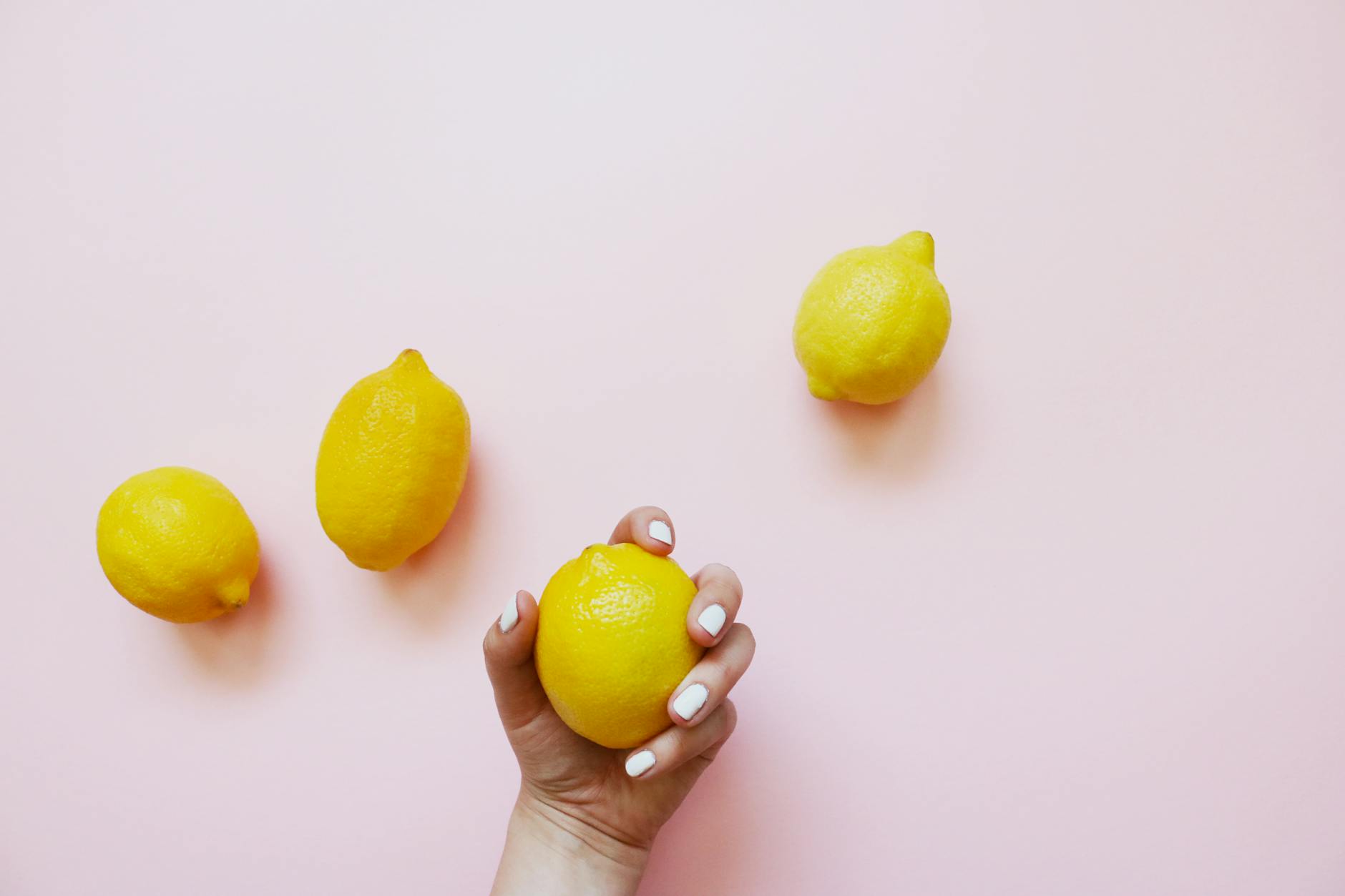 Hand holding a fresh lemon on soft pink background