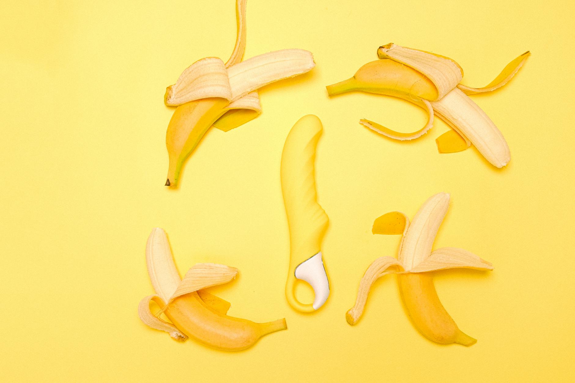 Yellow silicone lemon vibrator surrounded by fresh lemons on a bright yellow background