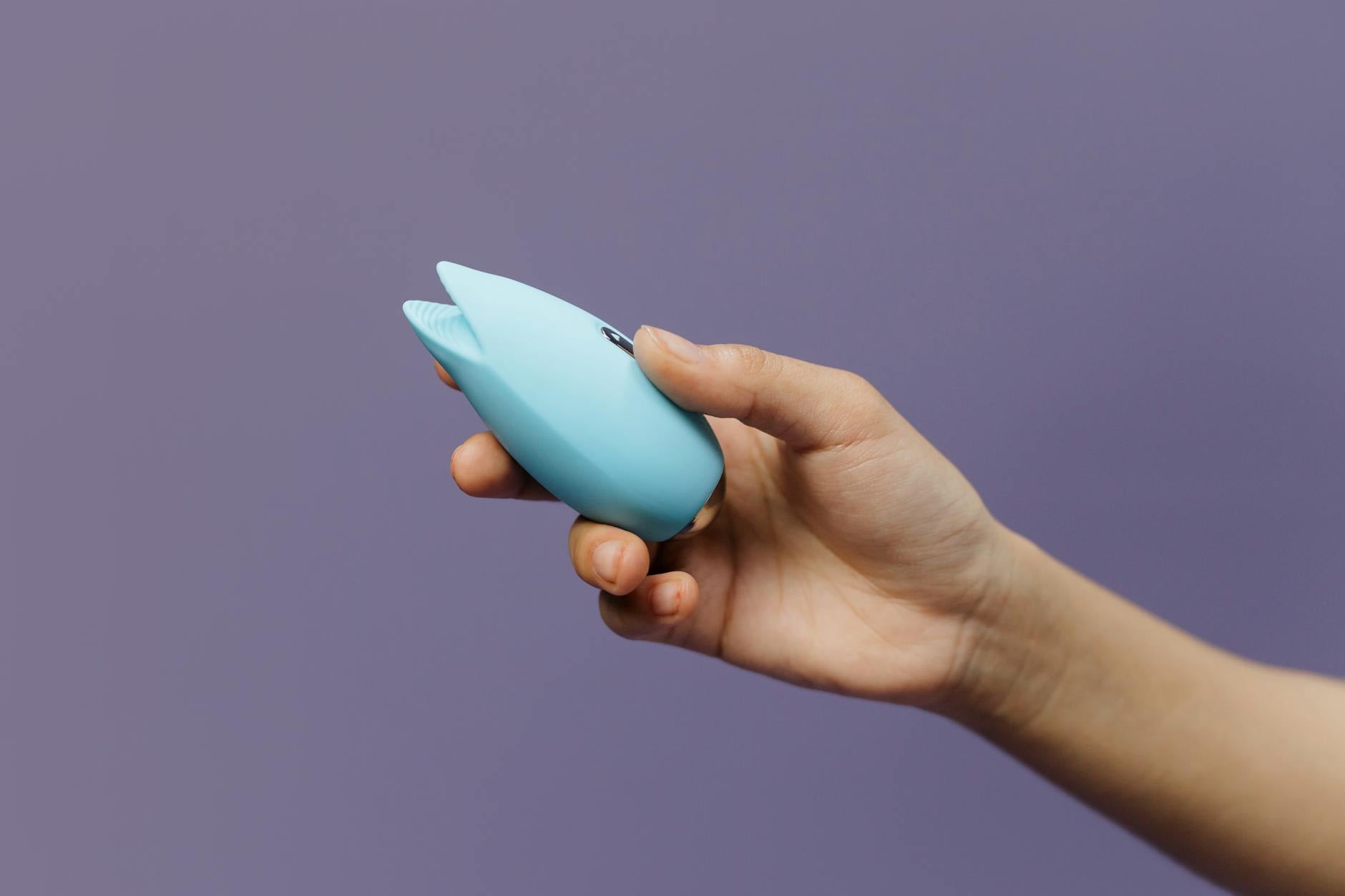 Hand reaching over colorful sex toys arranged on a table, representing choices in solo pleasure