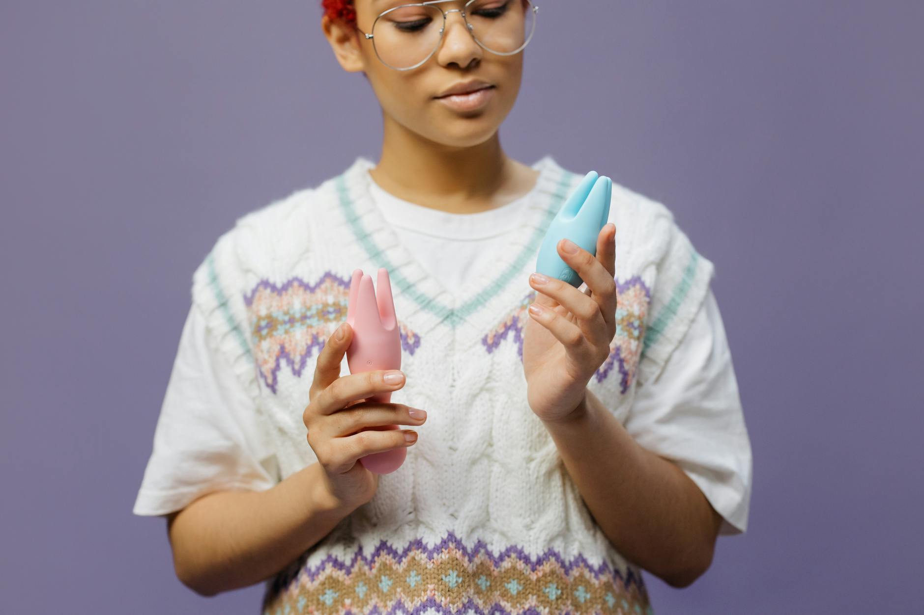 Woman holding blue and pink silicone vibrators contemplatively.