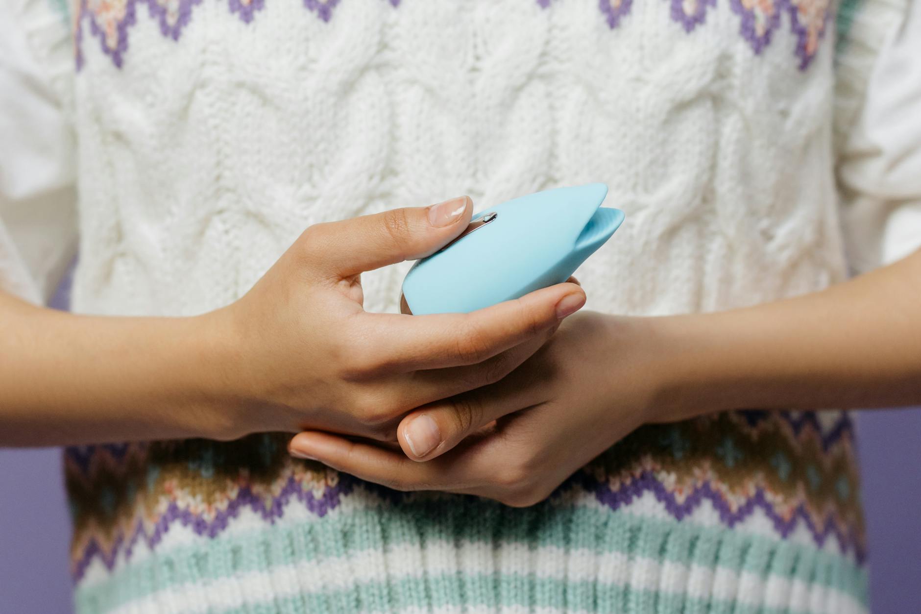 Hands holding a blue personal massager against a knitted sweater, symbolizing comfort and gentle reintroduction to pleasure.